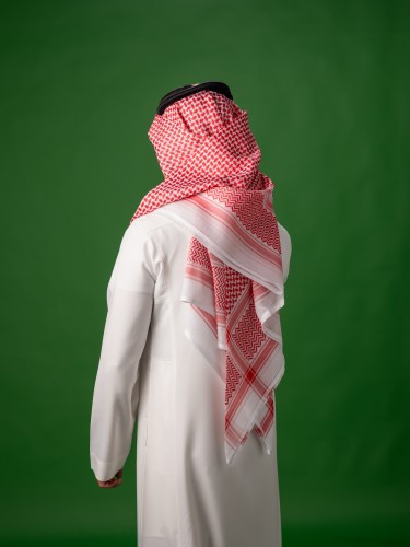 رجل يرتدي الزي الخليجي التقليدي باللون الأبيض والغترة الحمراء واقفًا على خلفية خضراء.