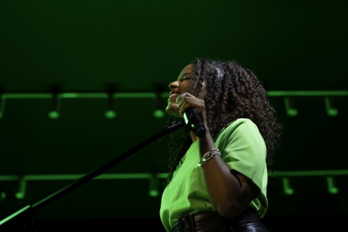 A woman sings and holds a microphone under green lights.