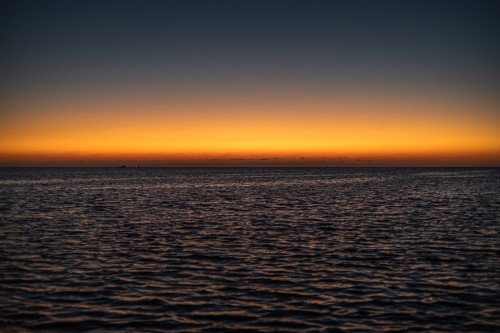 A view of the sunset over the sea with orange and golden color gradients on the horizon.