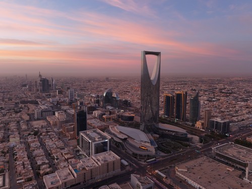 Aerial view of Riyadh city featuring the Kingdom Tower under a colorful sunset sky.