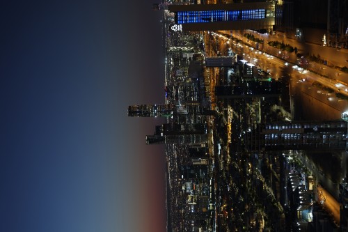 ** A nighttime cityscape image. The photo shows numerous skyscrapers illuminated with neon lights, with busy roads filled with cars. The sky is dark, enhancing the glow of the urban lights.\r\n\r\n**
