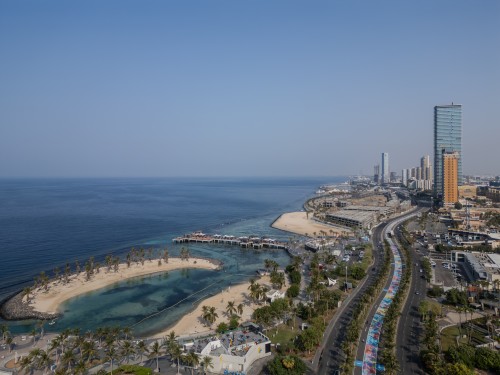 Aerial view of Jeddah Corniche showing the coastline, ocean, and tall buildings in the background.
