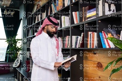 رجل سعودي يرتدي الزي السعودي التقليدي يتصفح أحد الكتب في المكتبة