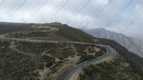 لقطة جوية سلسلة من الجبال الصخرية الشاهقة والطرق الوعرة الممتده بالجبل. تظهر السماء ملبدة بالغيوم وقت النهار.