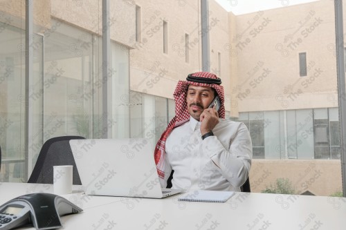 A Saudi man wearing the Saudi thobe sits in the meeting room and uses the mobile device