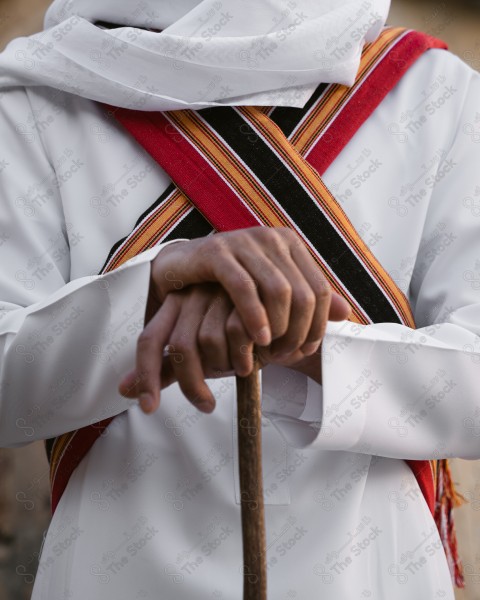 A snapshot of a Saudi man wearing traditional costume on the founding day, standing in front of a mud building and leaning on a stick, traditional costume, foundation day, ancient ancient buildings