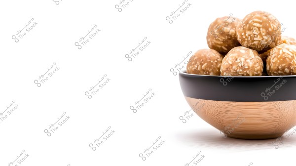 An image displays a collection of brown sweet balls with white pieces inside a dark wooden bowl with a black rim. The balls appear to be made from ingredients like nuts or coconut. The image has a simple composition with a white background.