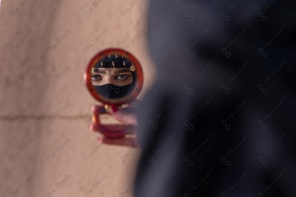 A shot of a Saudi woman whose eyes are reflected from the mirror wearing the traditional Saudi dress that represents the folklore, the day of foundation, the Saudi culture.