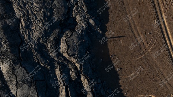 صورة جوية لتضاريس الحرة و اللابه البركانيه لنمطين مميزين من الأرض؛ الجانب الأيسر يعرض تضاريس داكنة وغير مستوية تشبه الصخور البركانية, بينما يظهر الجانب الأيمن أرض بذرات مفتوحة مع آثار إطارات ومستقيمات بارزة.