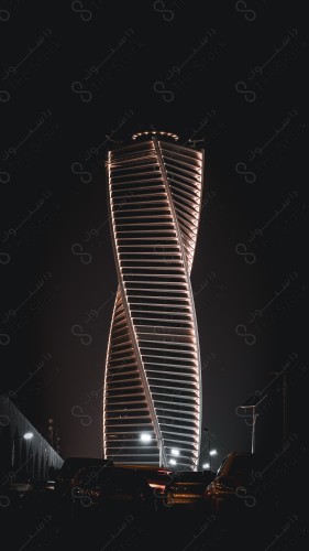 A shot of the braided tower glowing in bright yellow at night, buildings and landmarks in Riyadh.