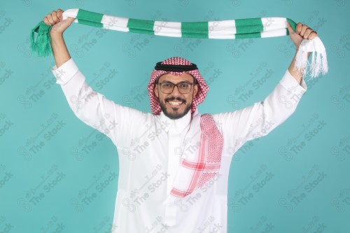 شاب سعودي يرتدي الزي السعودي ممسك شال بيده يقوم بتعابير وجه و يدين تدل على السعادة والحماس ، كأس العالم ، المنتخب السعودي.