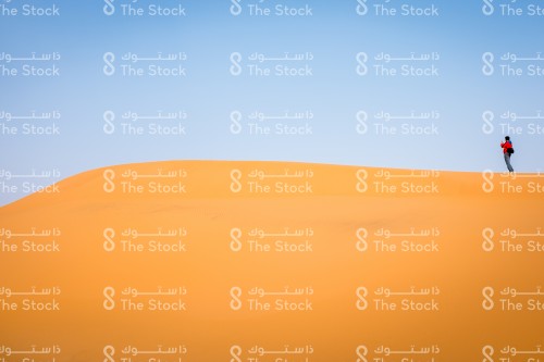 رجل يقف على جبل من الرمال و يتأمل صحراء خريص شرق المملكة العربية السعودية