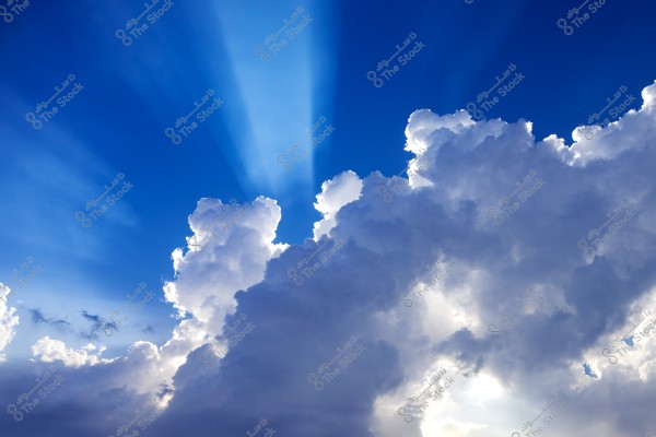 A clear blue sky with large white clouds, pierced by sun rays, creating a radiant glow and stunning illumination across the sky.