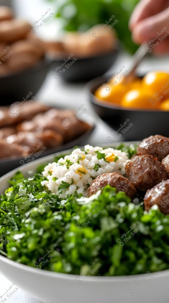 Image of a dish containing brown meatballs served with white rice topped with parsley and cilantro. There are also chopped greens like arugula. In the background, there are bowls containing fresh ingredients including cherry tomatoes and pieces of bread or meat.