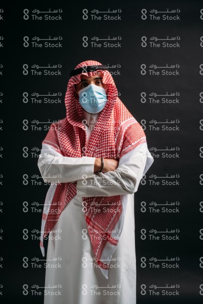 رجل بالزي السعودي يرتدي الكمامة على خلفية سوداء