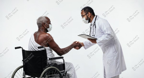 The image shows two men wearing medical masks. One man is seated in a wheelchair and is wearing casual white clothing that resembles Hajj attire. He is shaking hands with the other man, who is dressed in a white medical coat, holding a clipboard, and has a stethoscope around his neck. The setting appears to be a healthcare or hospital environment with a white and neutral background.