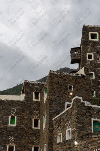 An ancient building built of stones in the middle of a group of windows surrounded by white paint while the sky looks cloudy during sunset, Rijal Almaa Heritage Village in the Asir region