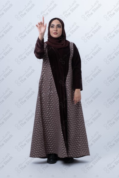 Portrait of a young Saudi woman wearing an abaya, with a smiling face, joyfully raising her finger, standing on a white background.