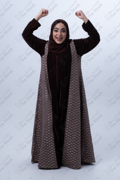 Portrait of a young Saudi woman wearing an abaya and hijab, with a smiling facial expression, standing against a white background