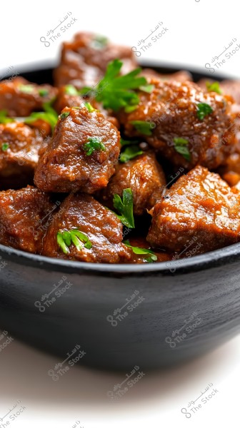 A black bowl filled with pieces of meat cooked in a dark sauce, garnished with fresh parsley. The dish is placed on a white surface with clear details of the shiny texture of the cooked meat.