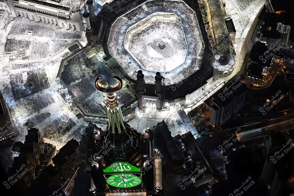 Aerial view of the Grand Mosque in Mecca at night, showing the Kaaba in the center of the crowded courtyard filled with pilgrims.