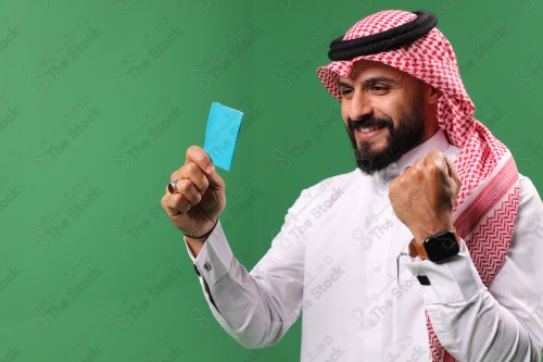 بورتريه رجل سعودي على خلفية خضراء متحمس يحمل بطاقة الصرافة مستعد للتسوق