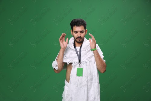 Portrait of a Saudi pilgrim on a green background wearing the Ihram to perform the Hajj rituals during prayer in several directions