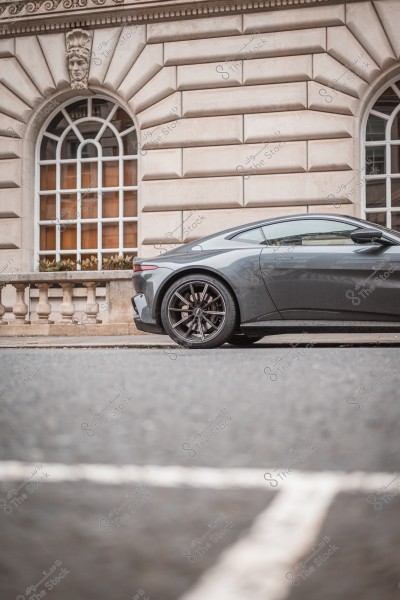 A grey sports car parked in front of a classical building with an ornate facade and arched windows.