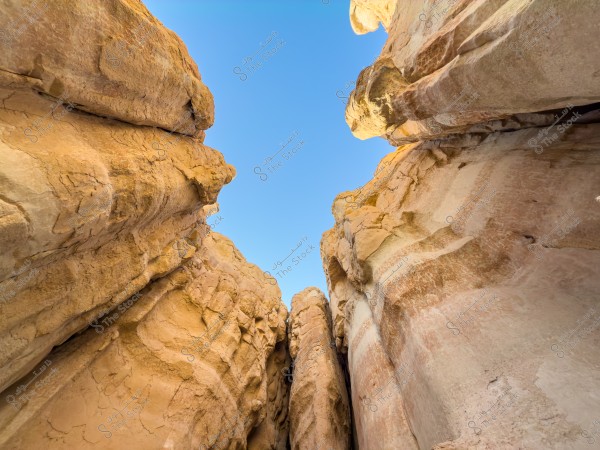 نظرة لأعلى إلى تشكيلات صخرية شاهقة ولونها أصفر فاتح تحت سماء زرقاء صافية, تبرز تفاصيل الصخور الطبيعية وألوانها المتنوعة.
-