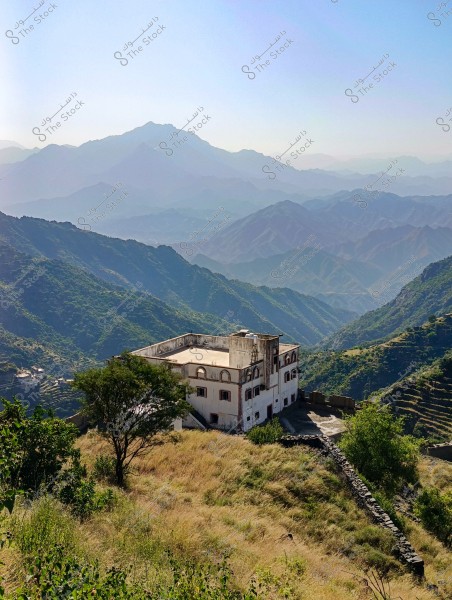 The image shows a scenic view of a mountainous area with layered mountains covered in greenery. In the foreground, there is a large, multi-story building with a traditional design situated on a hillside surrounded by trees and grass. The background features a range of high mountains that extend into the distance with various levels and shades.