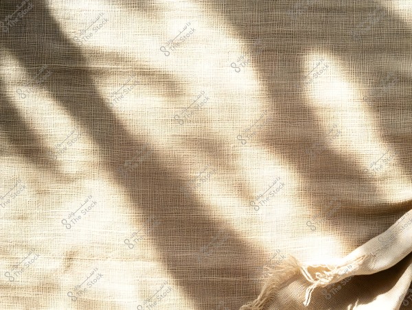An image showing a beige fabric with dark shadows running across it, suggesting the presence of natural light reflecting on the cloth. The bottom right edge of the fabric appears slightly frayed.