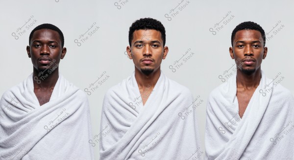 An image of three men looking directly at the camera. They are wearing white robe-like garments, suggesting a context such as baths or spas. The background is a neutral light gray, which highlights the subjects in the foreground.