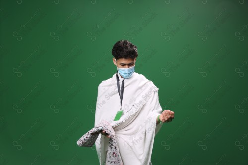 Portrait of a pilgrim with white skin on a green background, wearing Ihram to perform Hajj, carrying a prayer rug