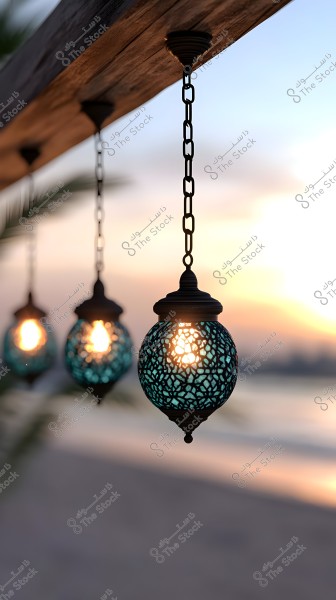 Several blue decorative glass lanterns hanging from chains under a wooden beam. The lanterns emit a warm glow, with a background of a beach, sea, and the soft light of a setting sun.