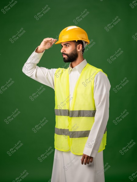 رجل يرتدي خوذة سلامة صفراء وسترة عمل عاكسة صفراء يقف أمام خلفية خضراء.