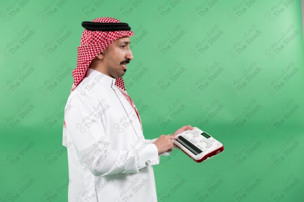 رجل "من ذوي الاعاقة" يرتدي الزي السعودي التقليدي يستخدم جهاز برايل على خلفية خضراء.