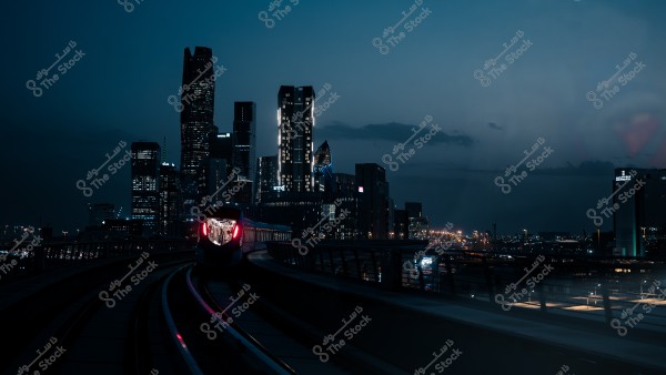 A train traveling on a track in a modern city at night, with skyscraper lights in the background.