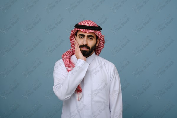 بورتريه شاب سعودي يرتدي الزي السعودي على خلفية سماويه يمسك رأسه ، يشعر بالصداع ،آلام الصداع والمرض.