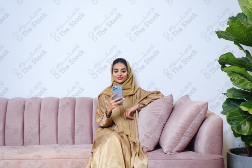 A Saudi girl sitting on the sofa and making different expressions using a mobile phone