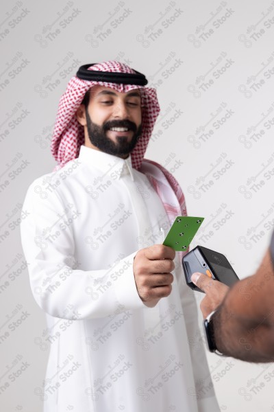 Portrait of a Saudi man holding a card and making automatic payments on a white background