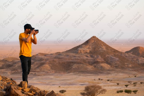 A shot of Mount Baloum and a person standing at the edge of a rock in one of the valleys in the Al-Rain region during sunset, nature in Saudi Arabia.