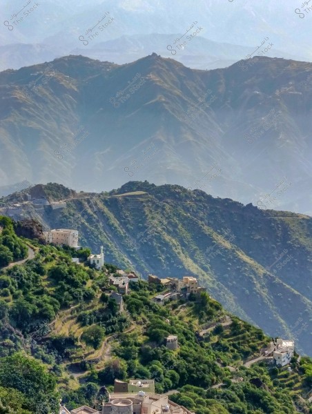 A beautiful landscape showing a cluster of houses scattered on the green mountain slopes in a mountainous area. The mountains extend in the background forming stunning gradients with sunlight casting shadows on the hills. The sky is clear blue above.