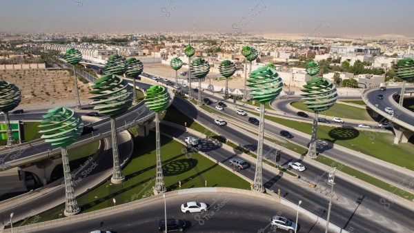 تصوير جوي لحركة سير السيارات على الطريق السريع في مدينة الرياض، الفن الهندسي المعماري للمجسمات الفنية على شكل أشجار خضراء، الطرق المتقاطعة في دوار عرقة بالمملكة العربية السعودية، البنية التحتية المتطورة