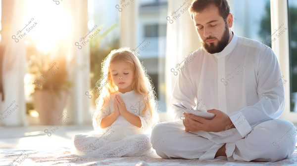 A man sits in a bright room wearing traditional white clothing, possibly a galabeya or Gulf thobe, next to a young girl dressed in a white outfit with lace details. The girl is in a meditative pose with her hands clasped in a prayer-like fashion. The scene conveys tranquility and calmness, with sunlight streaming in through the large window in the background.