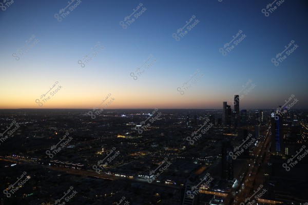 A nighttime cityscape displaying a skyline featuring a series of tall towers with various lights. The background sky presents a beautiful sunset gradient, transitioning from orange to deep blue, adding an enchanting effect to the city.
