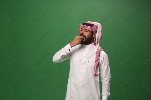 شاب سعودي على خلفية خضراء يرتدي الثوب و الشماغ، يقوم بعمل حركات بيده، يأكل الكعكة ، احتفالات العيد