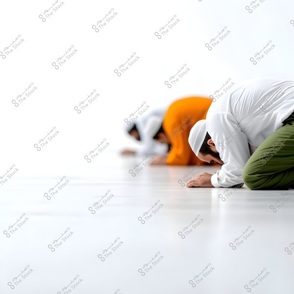 The image shows three individuals dressed in traditional clothing, performing the prostration position in prayer on a white floor. The nearest person is wearing a white shirt and green pants, with a white cap. The other two appear to be in white and orange garments.