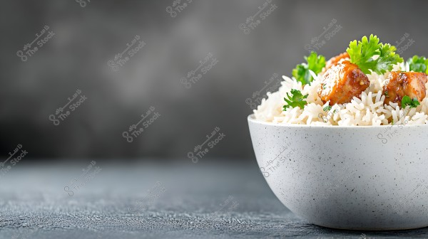 An image of a white bowl containing white rice garnished with pieces of cooked chicken and green parsley leaves. The background is dark and blurred, highlighting the details of the dish.