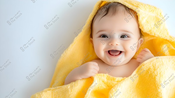 An image of a small baby smiling beautifully, wrapped in a soft yellow towel, conveying a sense of warmth and comfort. The background is clean and white, highlighting the joy in the baby’s expression and bright eyes.