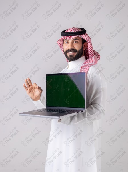 Portrait of a Saudi man holding a laptop, pointing at the laptop and making different expressions - green screen